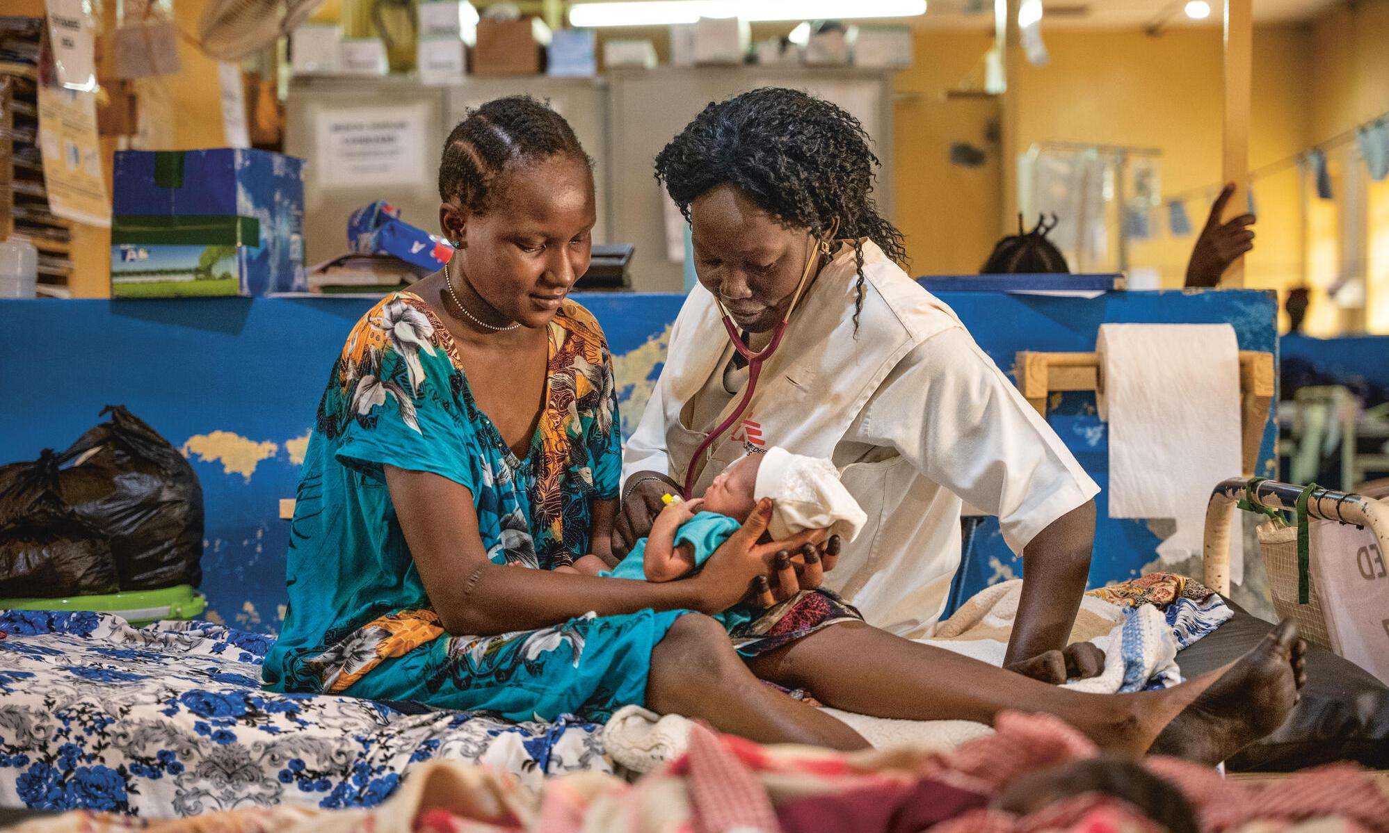An MSF nurse and patient sit on a hospital bed with a newborn baby in Aweil, South Sudan.